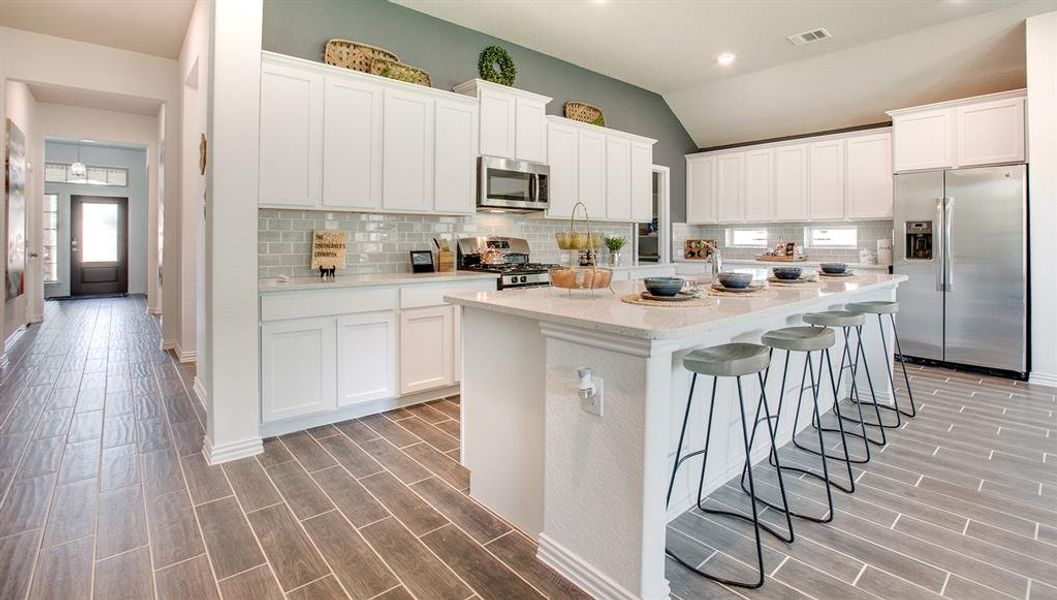 Kitchen with appliances with stainless steel finishes, a center island with sink, wood finish floors, a breakfast bar area, and lofted ceiling Kitchen with appliances with stainless steel finishes, a center island with sink, wood finish floors, a breakfast bar area, and lofted ceiling