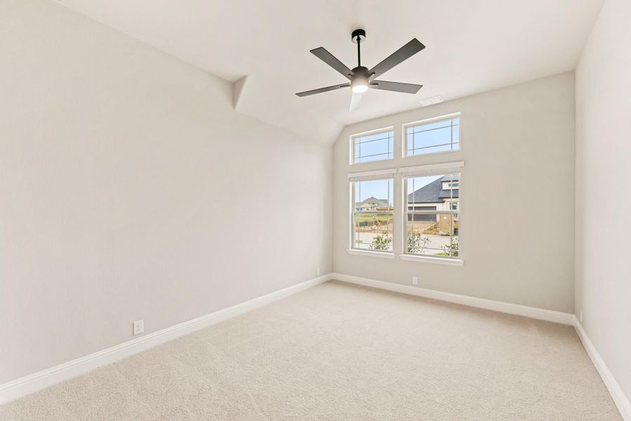 Empty bedroom with vaulted ceiling, ceiling fan, carpet flooring, and large windows with neighborhood view Empty bedroom with vaulted ceiling, ceiling fan, carpet flooring, and large windows with neighborhood view