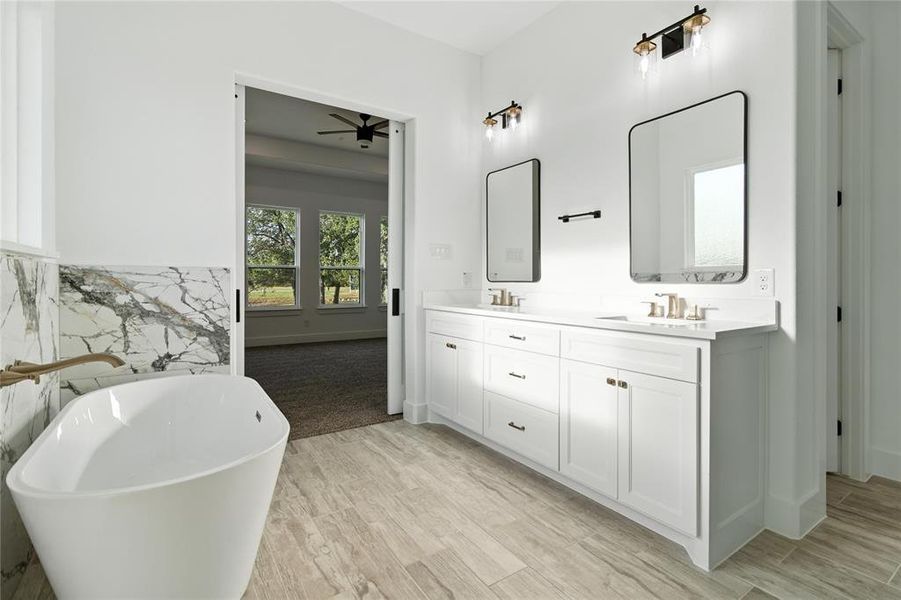 Full bath with double vanity, a freestanding tub, wood finished floors, and ceiling fan Full bath with double vanity, a freestanding tub, wood finished floors, and ceiling fan