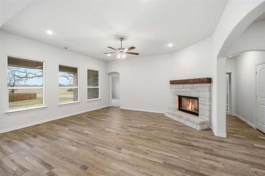 Unfurnished living room featuring arched walkways, a stone fireplace, light wood-type flooring, ceiling fan, and recessed lighting