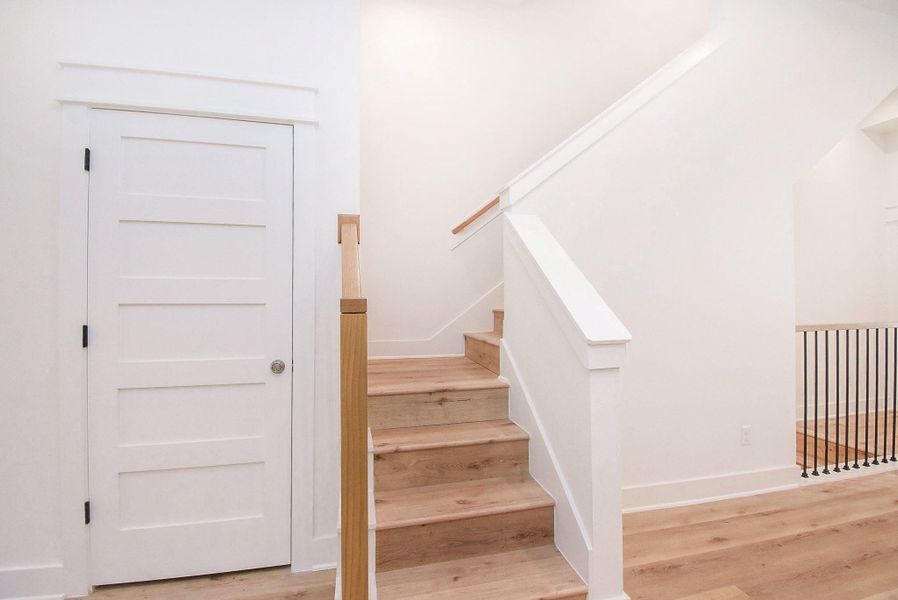 This photo shows a modern, minimalist staircase with light wood steps and white walls. There's a simple white door on the left, and the area is well-lit, giving a clean and spacious feel.