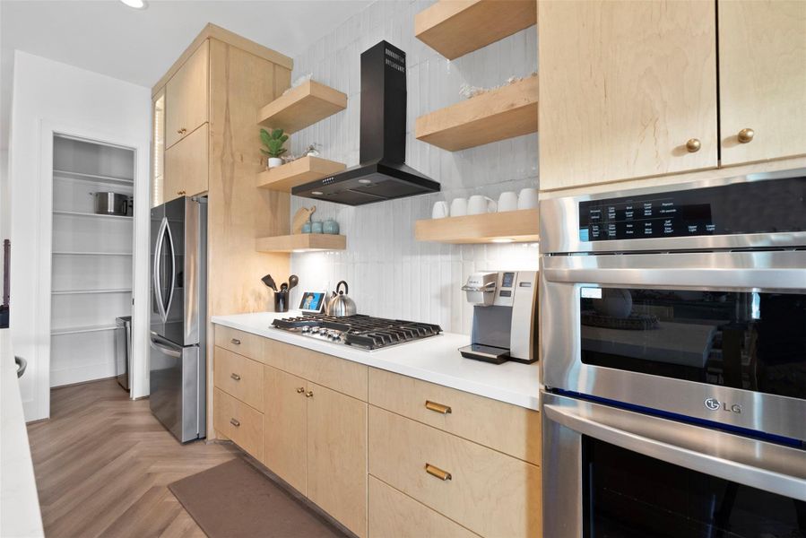 Centering on the sleek stovetop and stainless steel range hood, this view highlights the heart of the kitchen. Open wood shelves on either side add warmth and display space, while built-in appliances and a nearby coffee maker reflect both style and everyday ease. Centering on the sleek stovetop and stainless steel range hood, this view highlights the heart of the kitchen. Open wood shelves on either side add warmth and display space, while built-in appliances and a nearby coffee maker reflect both style and everyday ease.