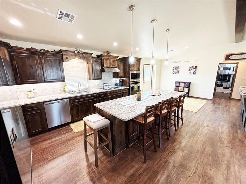 Kitchen featuring dark brown cabinetry, decorative backsplash, pendant lighting, a breakfast bar area, and light stone countertops Kitchen featuring dark brown cabinetry, decorative backsplash, pendant lighting, a breakfast bar area, and light stone countertops