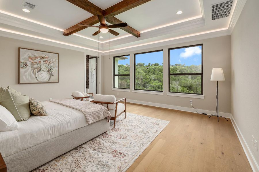Hardwood floors and a beamed ceiling with a fan enhance this naturally illuminated bedroom with scenic views.