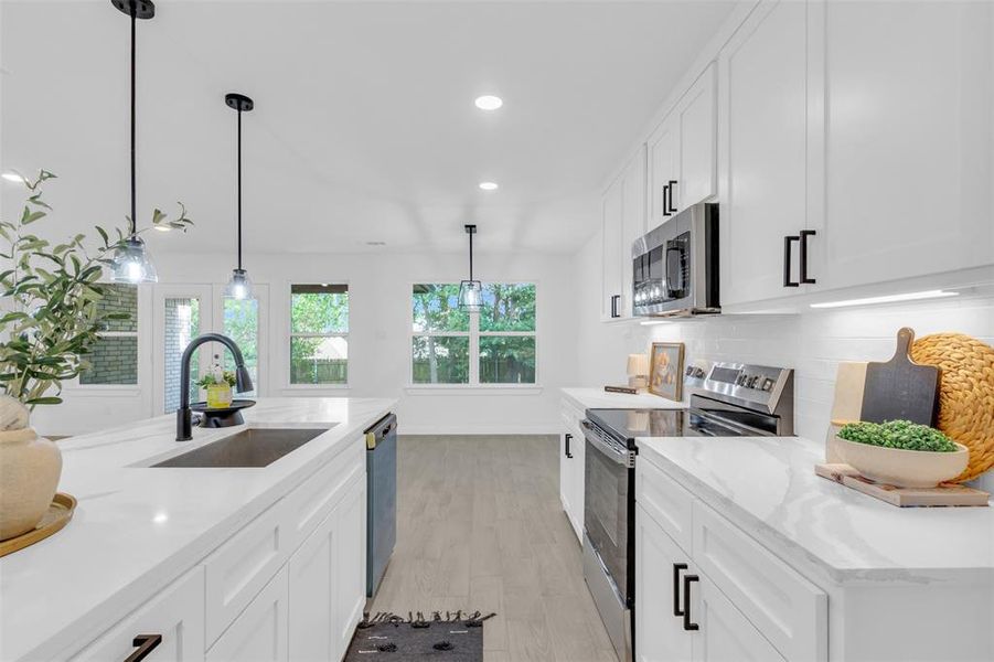 Kitchen featuring appliances with stainless steel finishes, backsplash, white cabinetry, light wood-type flooring, and recessed lighting
