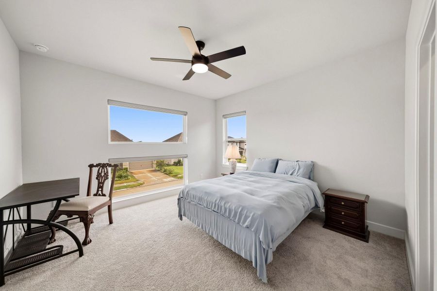 The third bedroom offers a comfortable, well-appointed retreat with plush carpet, a ceiling fan with integrated light, and front-facing windows dressed with roller shades for added privacy and precise light control.
