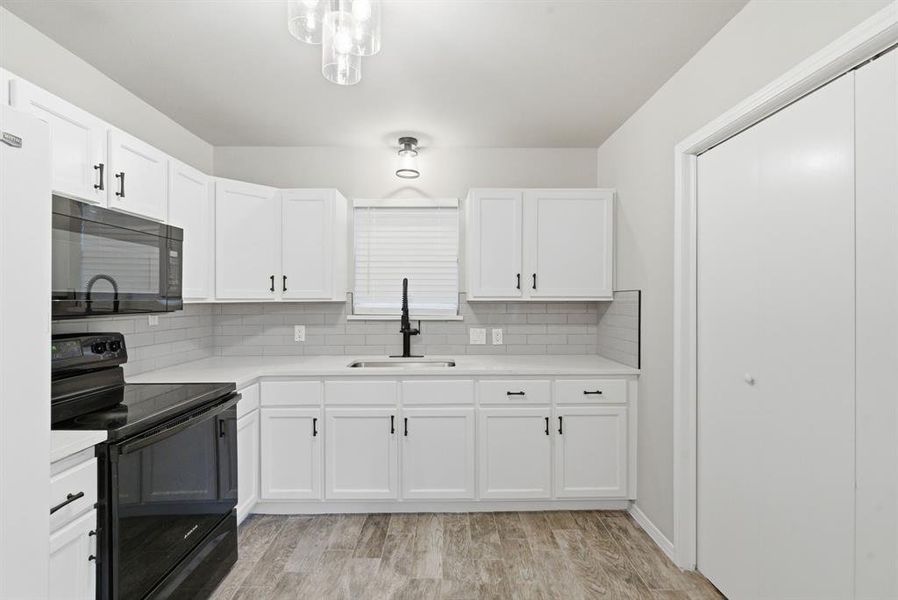 Kitchen featuring black appliances, light wood-type flooring, white cabinetry, and decorative backsplash Kitchen featuring black appliances, light wood-type flooring, white cabinetry, and decorative backsplash