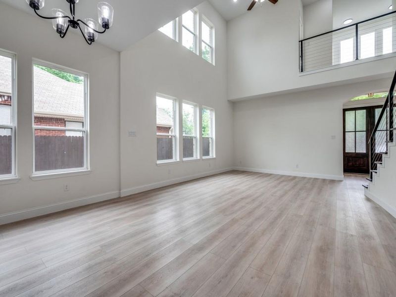 Unfurnished living room with a chandelier, stairway, plenty of natural light, a high ceiling, and light wood finished floors