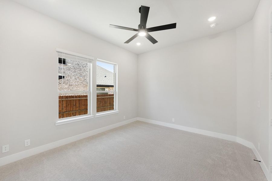 Empty bedroom with light carpet, white walls, black ceiling fan, and two windows
