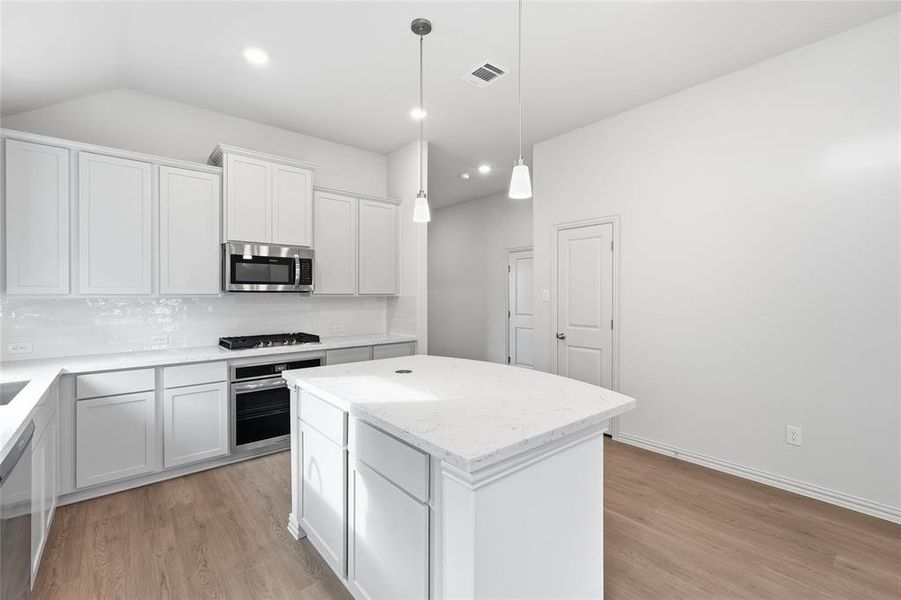 Kitchen with stainless steel appliances, light wood finished floors, a center island, light stone counters, and white cabinetry