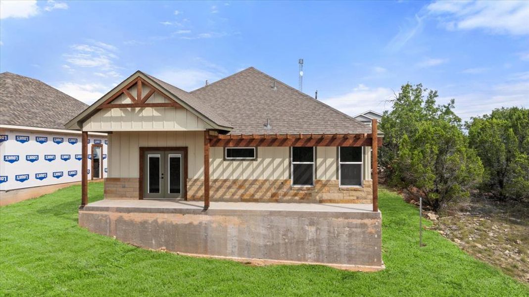 Back of house featuring a shingled roof, a porch, board and batten siding, a lawn, and stone siding Back of house featuring a shingled roof, a porch, board and batten siding, a lawn, and stone siding