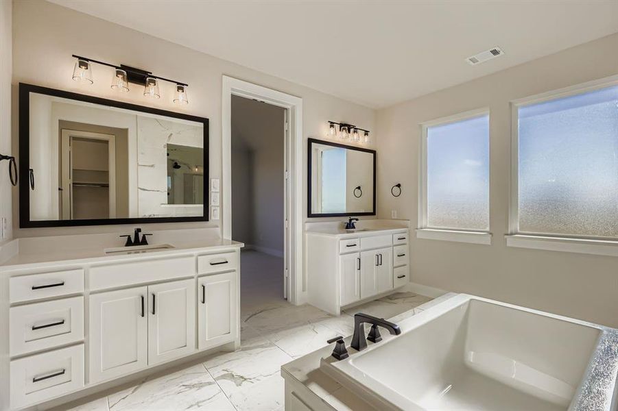 Bathroom with two vanities, light marble finish flooring, a stall shower, a garden tub, and a spacious closet