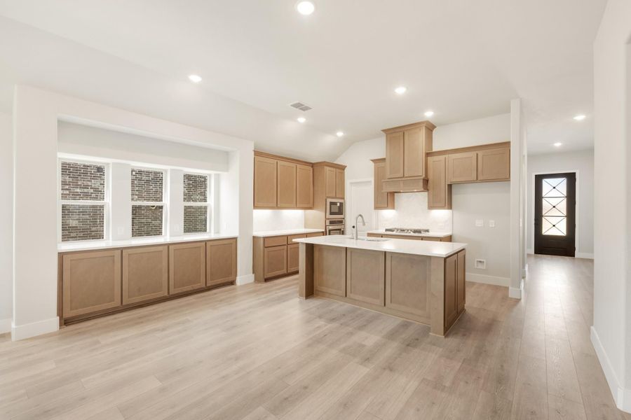 Open kitchen with tan wood cabinets, center island, white countertops, and light hardwood floors Open kitchen with tan wood cabinets, center island, white countertops, and light hardwood floors
