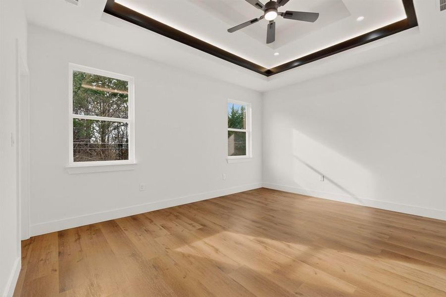 Empty room featuring a ceiling fan, light wood-type flooring, and a raised ceiling Empty room featuring a ceiling fan, light wood-type flooring, and a raised ceiling