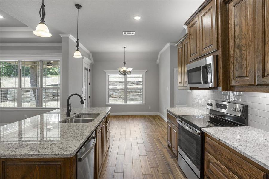 Kitchen featuring a center island with sink, backsplash, appliances with stainless steel finishes, sink, and crown molding