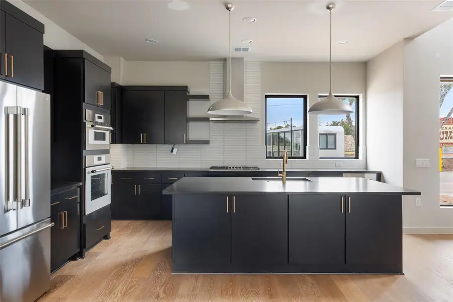 Kitchen featuring dark cabinetry, stainless steel appliances, a kitchen island with sink, light wood finished floors, and decorative backsplash