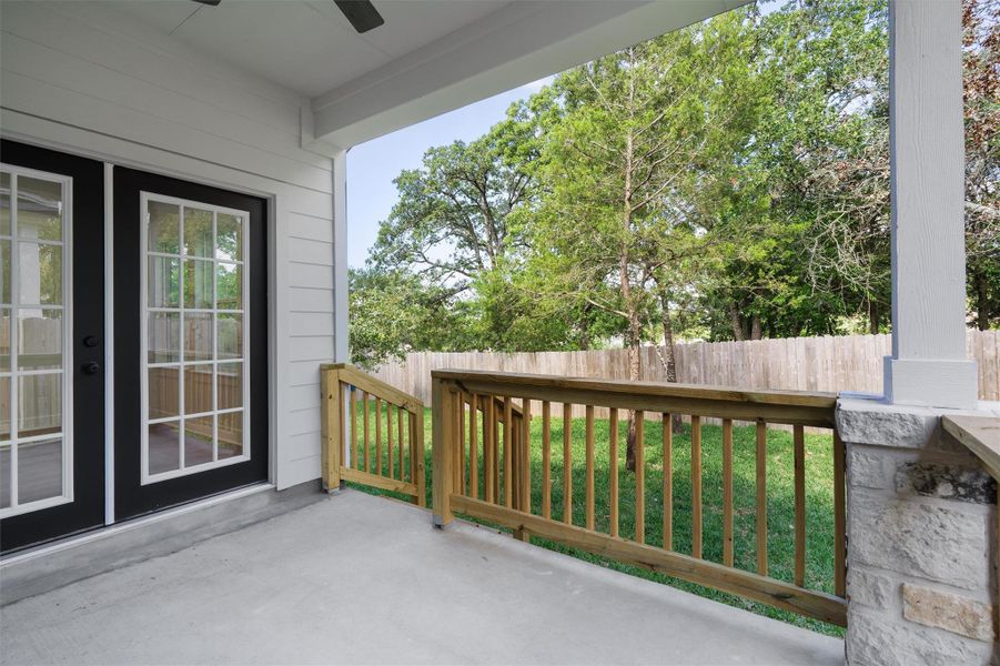 Covered concrete patio featuring twin black French doors, wood railings, and a stone column base