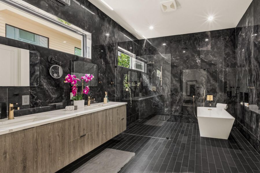 Expansive bathroom featuring floor-to-ceiling black marbled walls, a floating wood-finish double vanity with a light-toned countertop, and a rectangular freestanding soaking tub