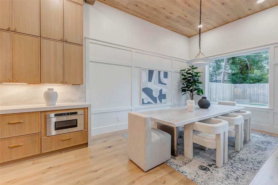 Creating a warm and inviting space for entertaining, this beautifully appointed dining room features floor-to-ceiling millwork, natural wood flooring, a stunning wood-clad ceiling with recessed lighting, and large picture windows.