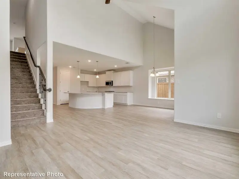 Spacious open-concept living area featuring light-colored flooring, high ceilings, and a view of the kitchen with white cabinetry and a large island