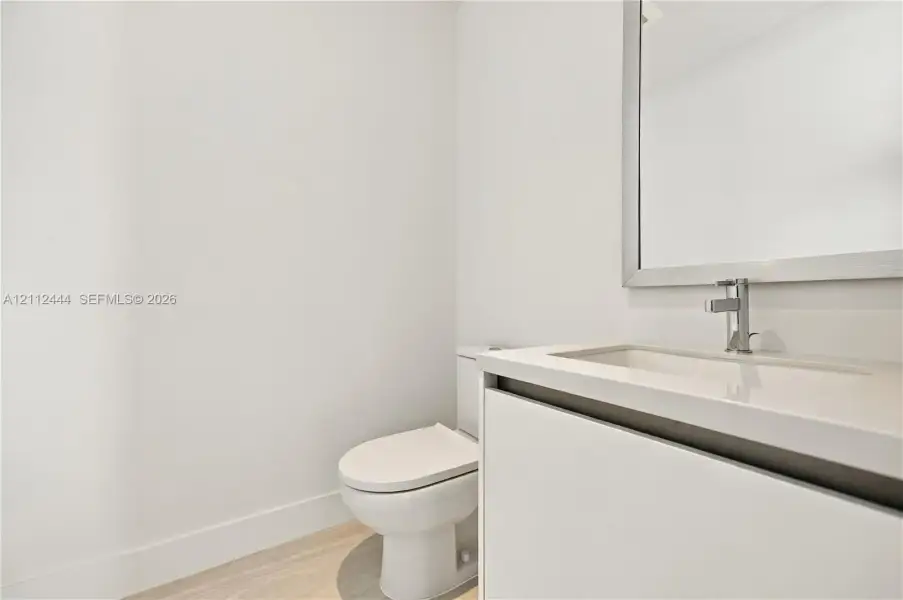 Modern vanity featuring a seamless integrated countertop and sink, wall-mounted mirror with a metallic frame, chrome faucet, and light-toned wood-finish flooring