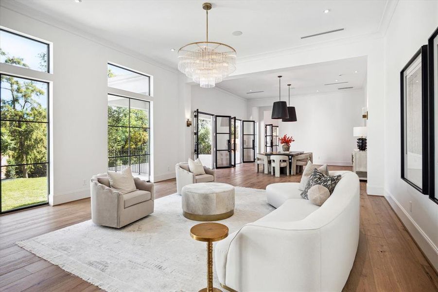 This expansive great room seamlessly combines a luxury bar, sophisticated living room, and formal dining area, offering an ideal space for entertaining. Durango Doors open to the covered patio, extending the elegance outdoors. White oak flooring anchors the space, while stunning designer lighting adds a touch of brilliance from above.