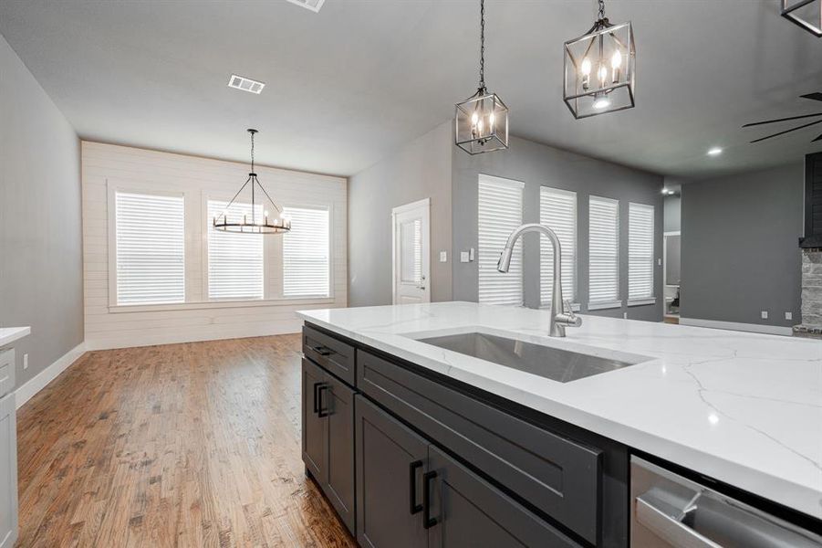 Kitchen with visible vents, pendant lighting, light stone countertops, a sink, and an inviting chandelier Kitchen with visible vents, pendant lighting, light stone countertops, a sink, and an inviting chandelier