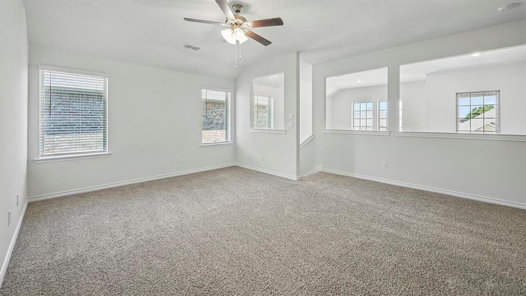 Spacious carpeted room featuring a ceiling fan, multiple windows with blinds, and decorative interior wall cutouts