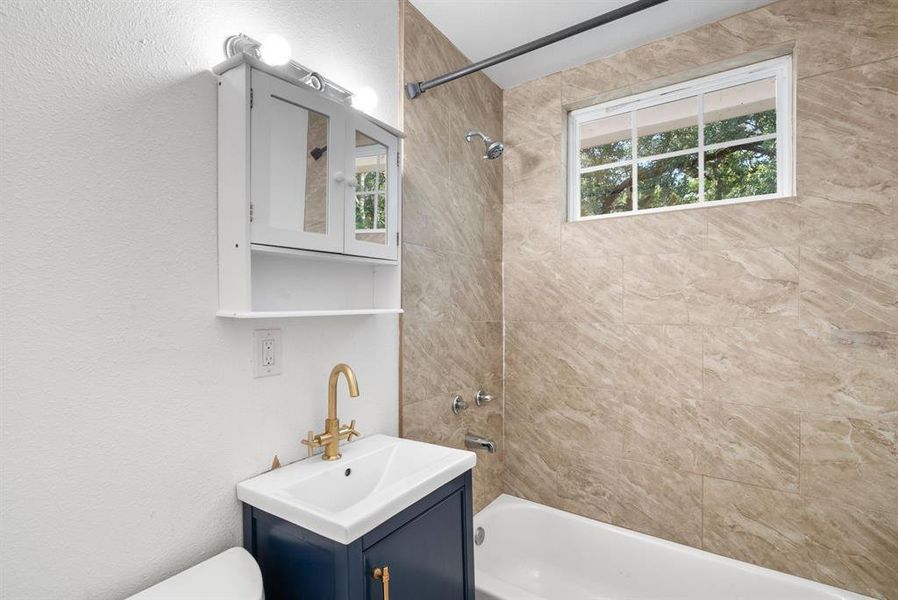 Full bathroom with a wealth of natural light, tiled shower / bath combo, vanity, and toilet