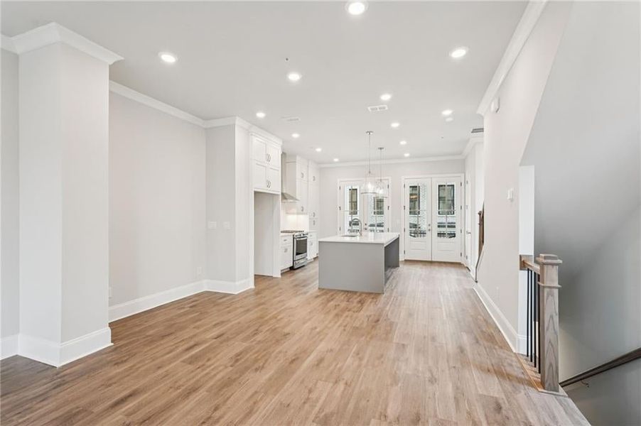 Kitchen featuring a kitchen island with sink, hanging light fixtures, crown molding, french doors, and light wood finished floors