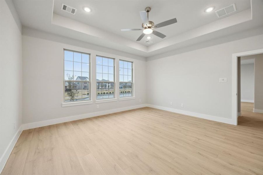 Empty room featuring ceiling fan, a raised ceiling, and light hardwood / wood-style flooring