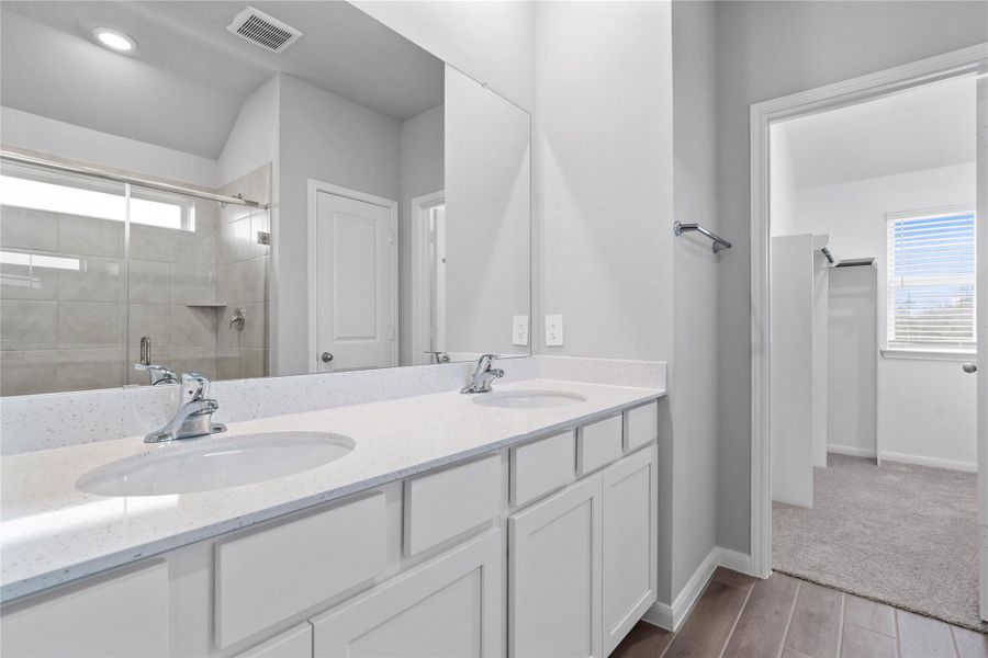 A bright and functional primary bath offering dual sinks for busy mornings, a large mirror, and a modern glass-enclosed shower, creating a serene and efficient space.