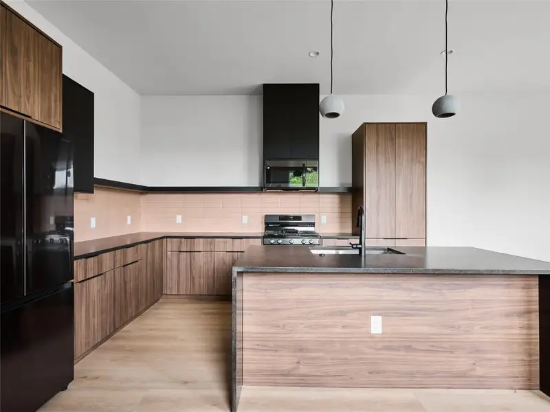 Kitchen featuring stainless steel appliances, hanging light fixtures, decorative backsplash, a kitchen island with sink, and dark stone countertops Kitchen featuring stainless steel appliances, hanging light fixtures, decorative backsplash, a kitchen island with sink, and dark stone countertops