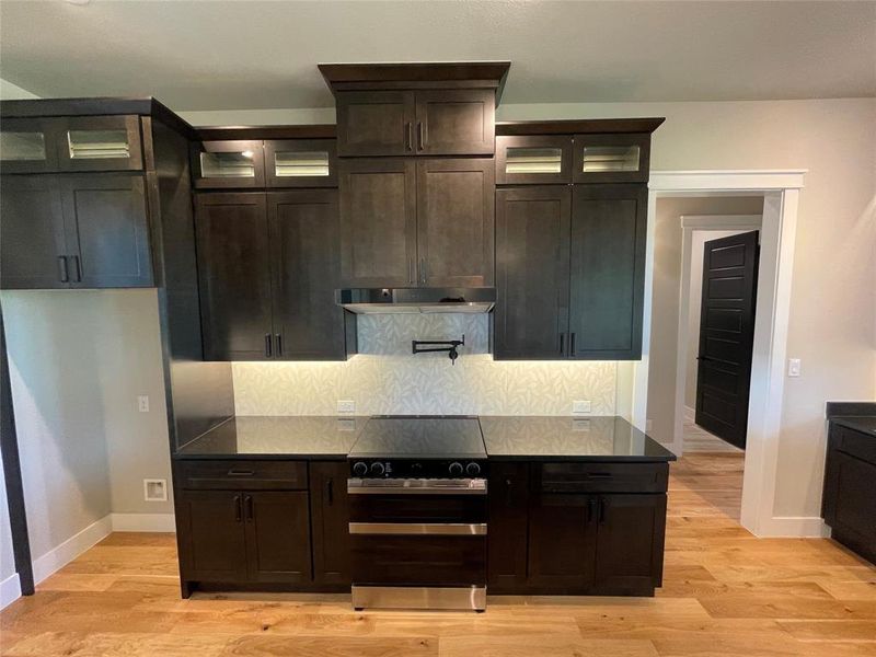 Kitchen featuring dark wood cabinetry with crown molding, glass-front upper cabinets, and under-cabinet lighting