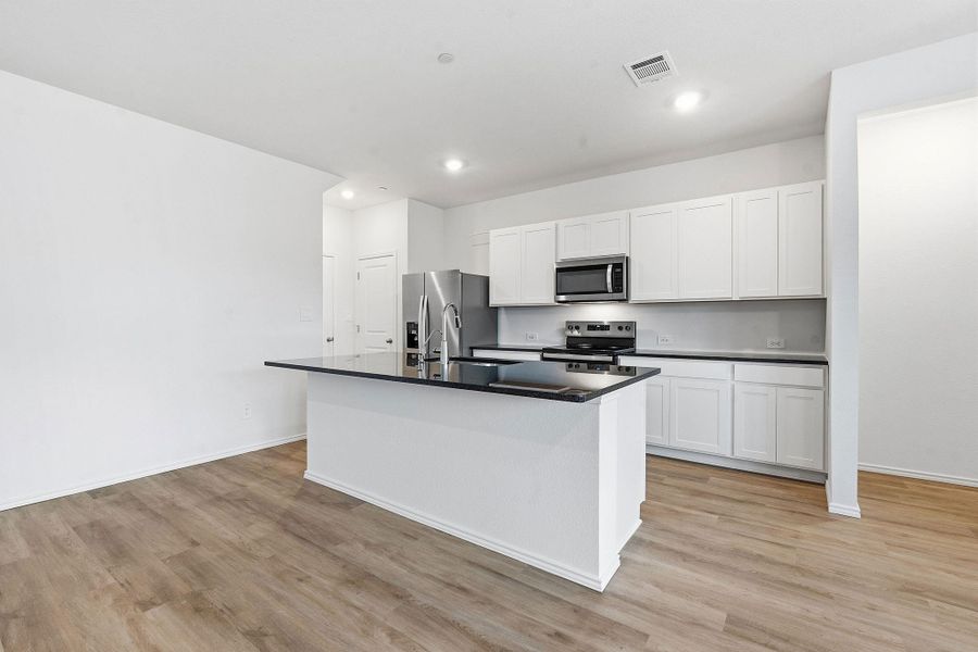 Open-concept kitchen featuring an island with a black countertop, white shaker-style cabinetry, stainless steel appliances, and wood-finish flooring