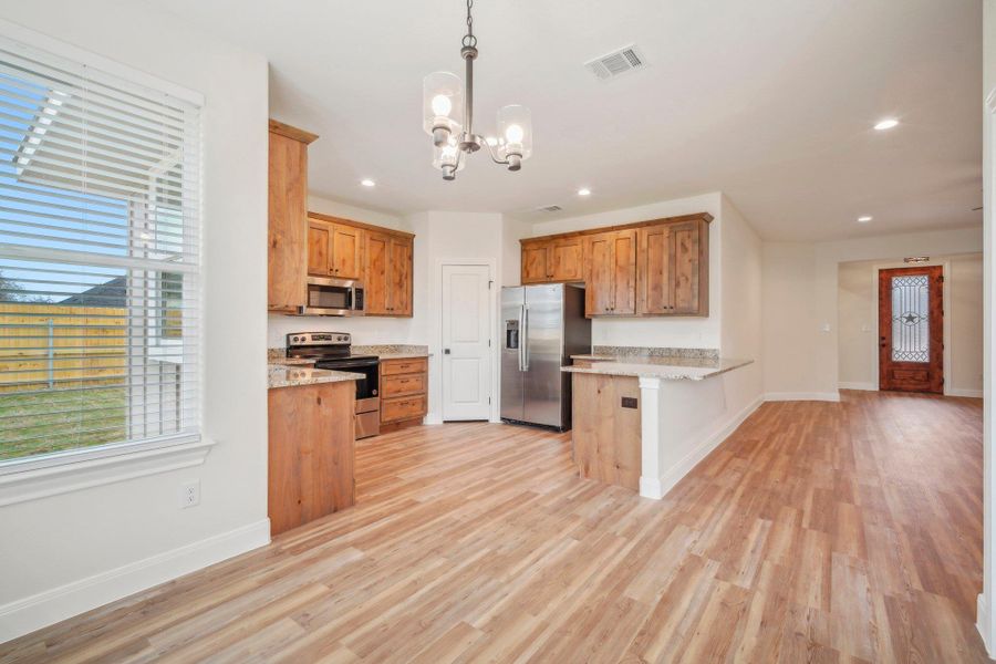 Kitchen featuring visible vents, brown cabinets, stainless steel appliances, a peninsula, and a chandelier