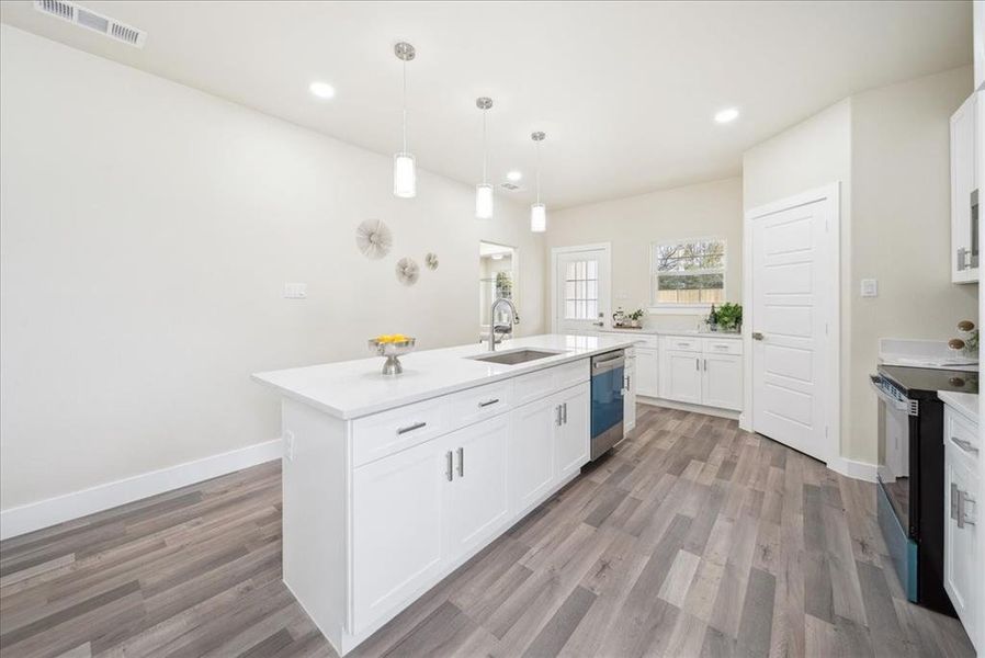 Kitchen with stainless steel dishwasher, white cabinets, light hardwood / wood-style floors, black range with electric stovetop, and an island with sink