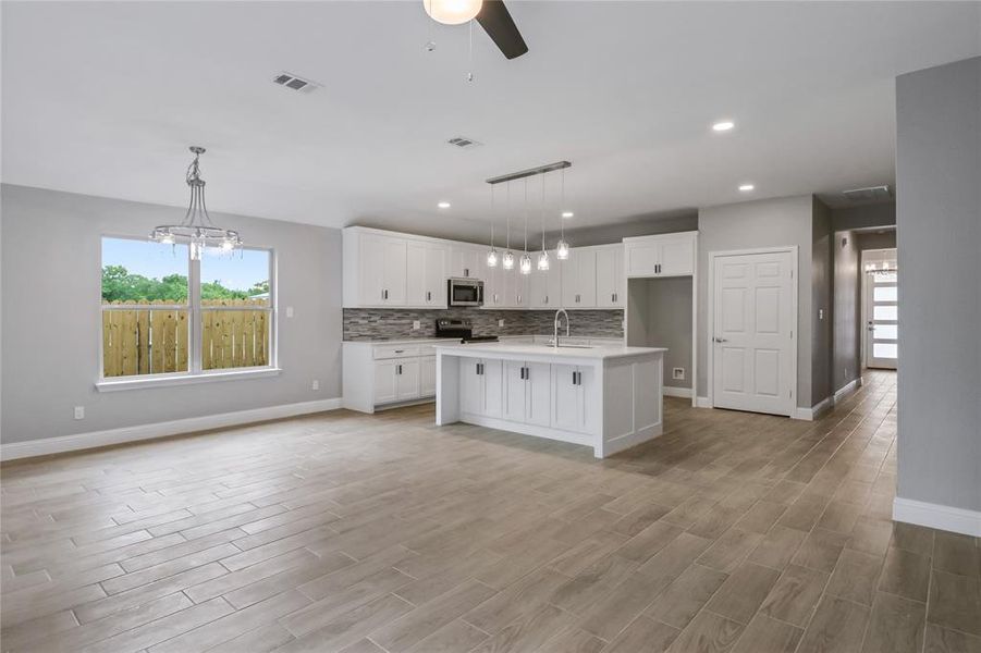 Kitchen featuring stainless steel appliances, white cabinets, sink, backsplash, and a kitchen island with sink