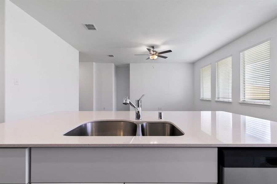 Kitchen with sink, ceiling fan, dishwasher, and light stone counters