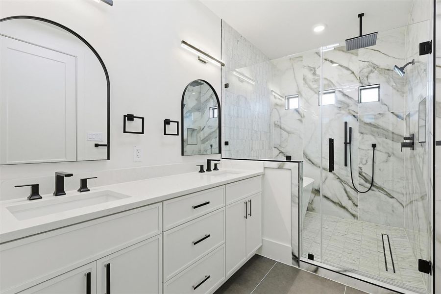 An ensuite bathroom provides a double vanity with arched mirrors and a large glass-enclosed shower with multiple showerheads.