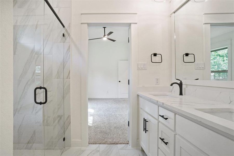 Bathroom with a marble finish shower, double vanity, light colored carpet, and ceiling fan
