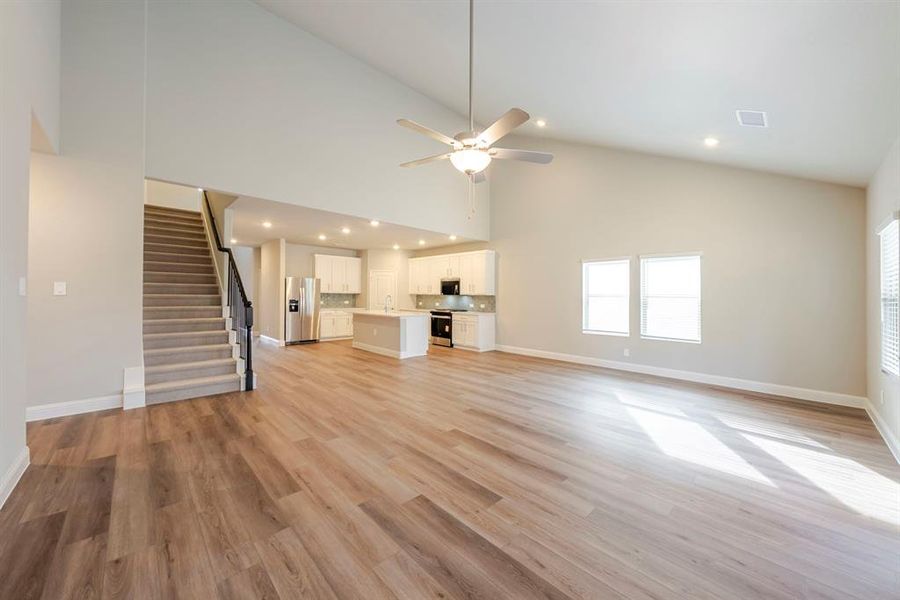 Unfurnished living room with stairway, light wood-style flooring, ceiling fan, recessed lighting, and high vaulted ceiling Unfurnished living room with stairway, light wood-style flooring, ceiling fan, recessed lighting, and high vaulted ceiling