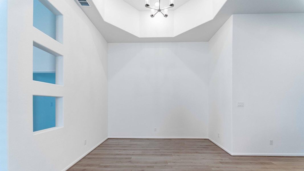 Empty room with light wood-style flooring, a chandelier, and a raised ceiling