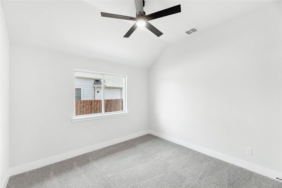 Empty bedroom with gray carpet, vaulted ceiling, black ceiling fan, and single window