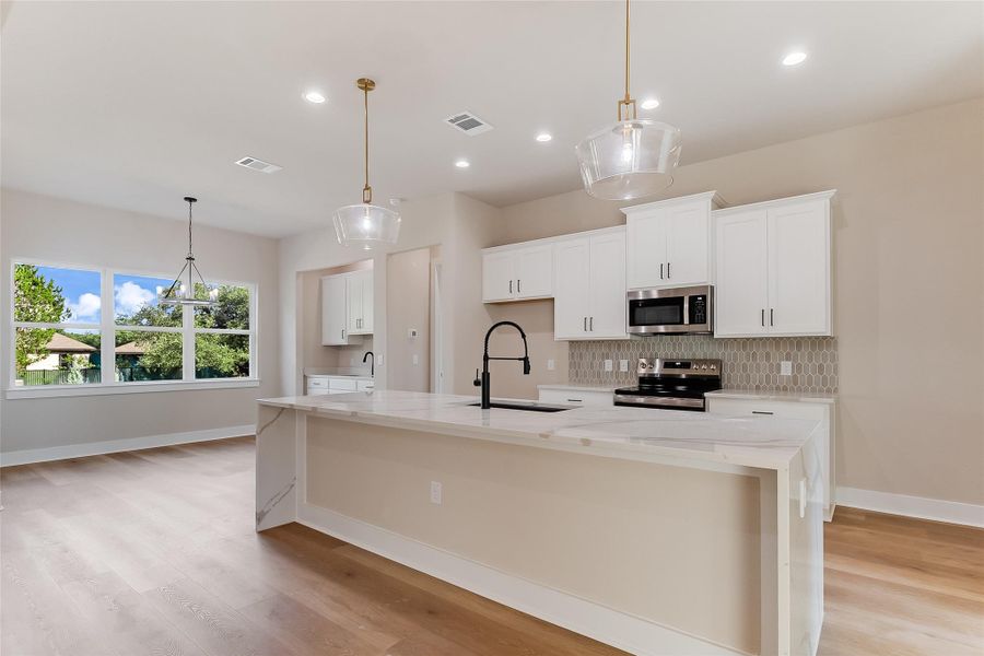 Kitchen with light stone counters, backsplash, pendant lighting, an island with sink, and recessed lighting Kitchen with light stone counters, backsplash, pendant lighting, an island with sink, and recessed lighting