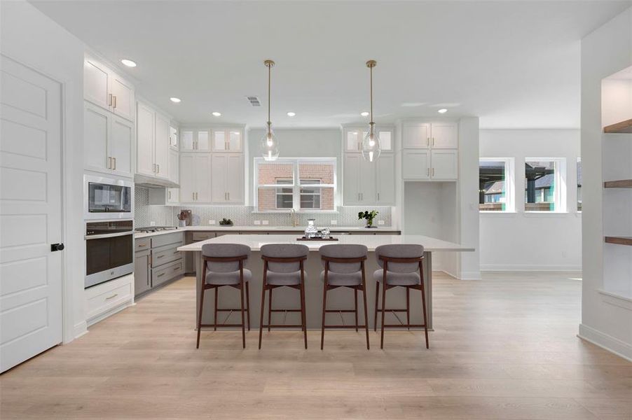 Dual tone kitchen with a breakfast bar, a center island, stainless steel appliances, decorative light fixtures, and backsplash