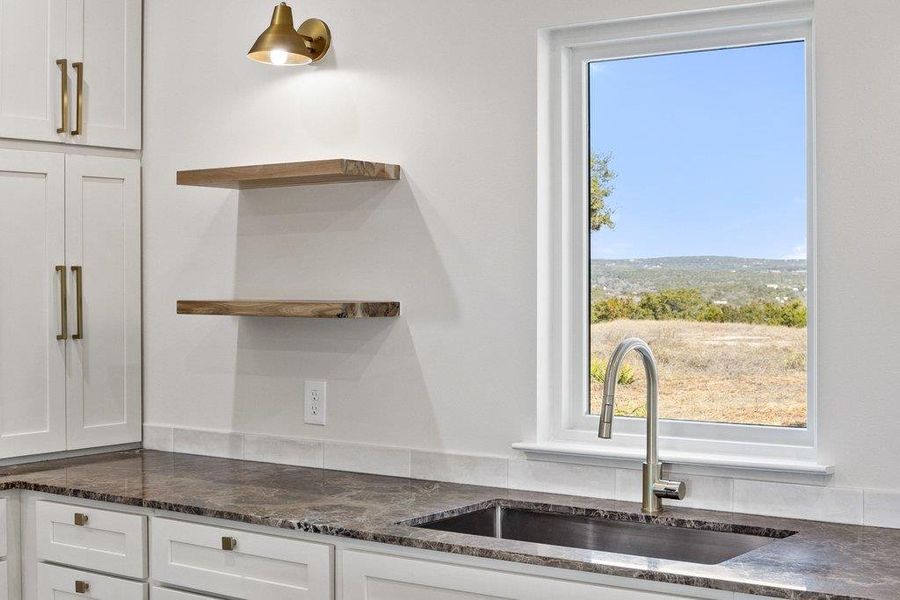 Kitchen view of open shelves, white cabinetry, and dark stone countertops