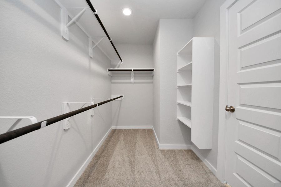 Walk-in closet that epitomizes luxury and practicality. This generously sized space features built-in shelving, offering abundant room for impeccable organization. High ceilings and recessed lighting create a bright and welcoming ambiance. Sample photo of completed home with similar floor plan. Actual colors and selections may vary.