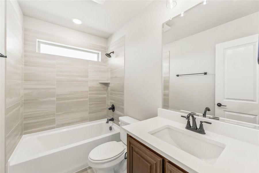 Bathroom with tub-shower combo, large tile surround, white vanity with dark wood cabinet, and toilet Bathroom with tub-shower combo, large tile surround, white vanity with dark wood cabinet, and toilet