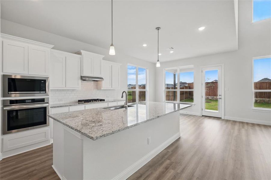 Kitchen featuring a kitchen island with sink, dark wood finished floors, a sink, stainless steel appliances, and white cabinetry Kitchen featuring a kitchen island with sink, dark wood finished floors, a sink, stainless steel appliances, and white cabinetry
